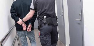 Officer escorting handcuffed person down hallway.