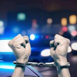 Handcuffed fists raised in front of police lights.