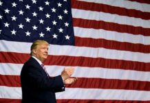 Man clapping in front of large American flag