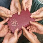 Hands holding a closed red Bible together