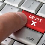 Finger pressing red delete key on keyboard