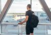Person with backpack at airport window watching airplanes