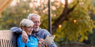 Older couple sitting on bench using tablet outdoors
