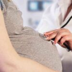 Doctor uses stethoscope on pregnant woman's belly.
