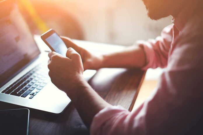 Person using smartphone and laptop at desk