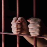 Hands gripping red jail bars tightly