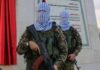 Masked soldiers holding rifles in front of a monument