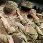 Soldiers in camouflage uniforms saluting in formation outdoors