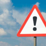 Warning sign with exclamation mark against cloudy sky