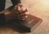 Hands praying on a Bible