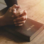 Hands praying on a Bible