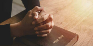 Hands praying on a Bible