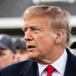 Man in suit and red tie speaking outside