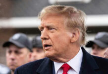 Man in suit and red tie speaking outside
