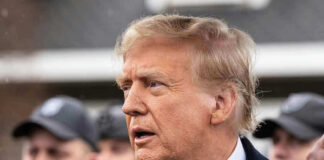 Man in suit and red tie speaking outside