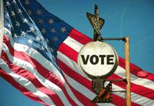 A vintage 'Vote' sign in front of an American flag