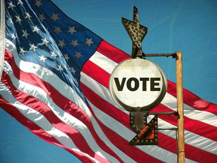 shutterstock_185810546.jpg A vintage 'Vote' sign in front of an American flag