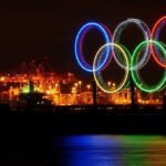 Illuminated Olympic rings displayed at night over a harbor