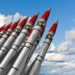 A row of military missiles with red tips and nuclear symbols against a blue sky