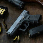 Handgun with ammunition, magazine, and rifle on wooden table.