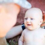 A smiling baby interacting with a parent in a military uniform