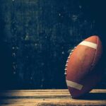 An American football resting on a wooden surface against a dark background