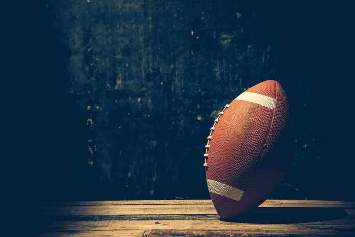 An American football resting on a wooden surface against a dark background