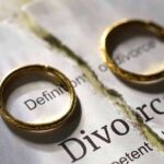Two gold wedding rings placed on a torn page with the word 'Divorce'