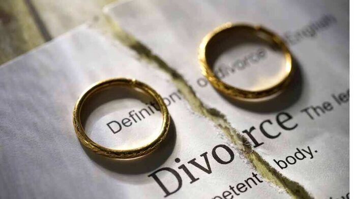 Two gold wedding rings placed on a torn page with the word 'Divorce'