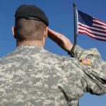Soldier in military uniform saluting in front of an American flag