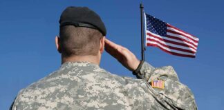 Soldier in military uniform saluting in front of an American flag