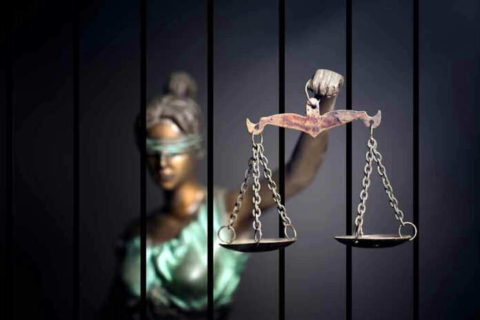 Blindfolded Lady Justice statue holding scales behind bars.