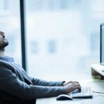 Man sitting at a desk, looking up while typing on a computer