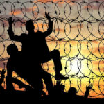 Silhouettes of people climbing barbed wire fence.