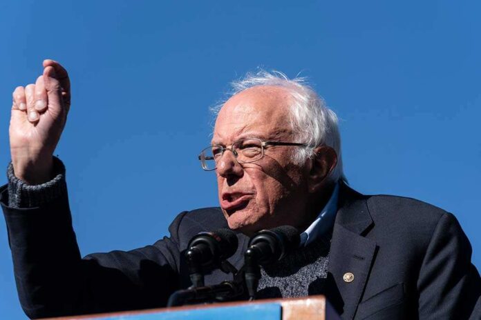 Bernie Sanders passionately speaking at a rally against a clear blue sky