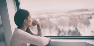A young woman sitting by a window, looking out thoughtfully