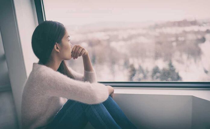 A young woman sitting by a window, looking out thoughtfully