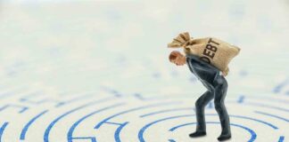 A miniature businessman carrying a sack labeled 'DEBT' in a maze