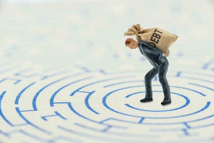 A miniature businessman carrying a sack labeled 'DEBT' in a maze