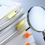 Stack of documents with a magnifying glass beside it