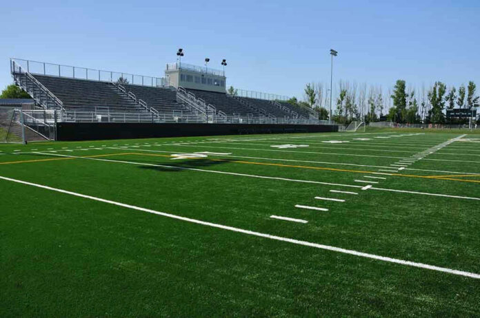 Empty football field with bleachers in background.