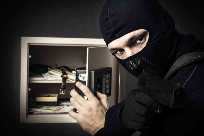 shutterstock_122674900.jpg A masked burglar holding a gun while attempting to open a safe