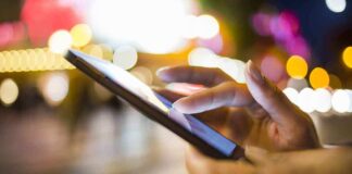 A persons hand using a smartphone in a city at night with blurred lights in the background