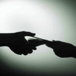 Zelensky’s BRIBE Scandal Explodes Silhouette of hands exchanging money in dim light.