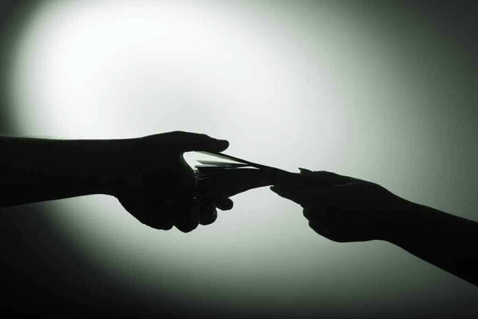 Silhouette of hands exchanging money in dim light.