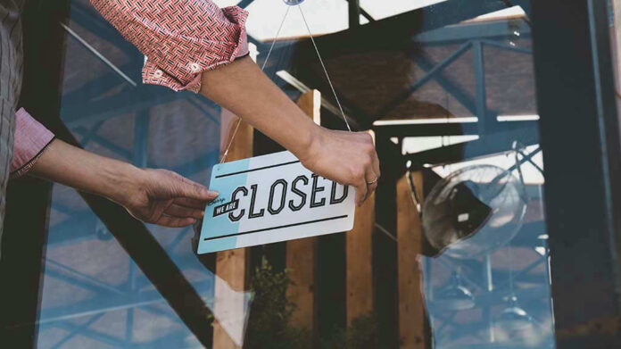 Hand placing closed sign on glass door