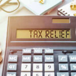 Calculator display reads TAX RELIEF amidst coins and glasses.