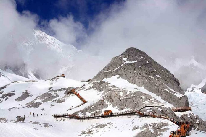 shutterstock_106809467.jpg Snow-covered mountain with hiking trails and tourists under a cloudy sky