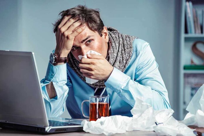 A man looking stressed and unwell while working on a laptop