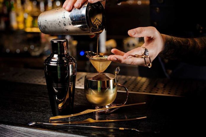 Bartender pouring a cocktail through a strainer into a gold cup